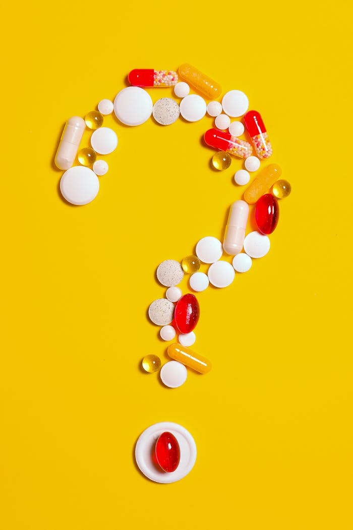 about-img A creative arrangement of various pills forming a question mark against a bright yellow background.